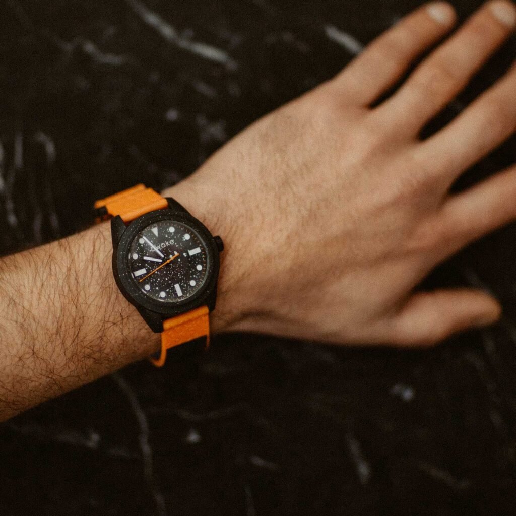 This image features an Awake concept eco friendly watch made from recycled fishing nets, the watch is orange with a black watch face and on a mans wrist