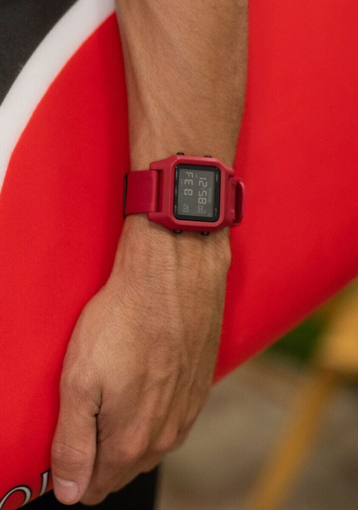 Nixon surf watch in pink shown on surfer holding a surf board