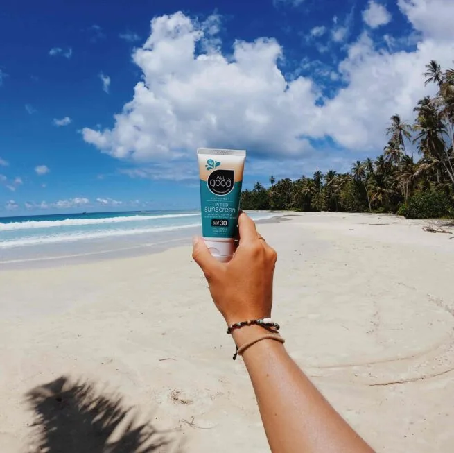 Arm holding All good cruelty free sunscreen on beach